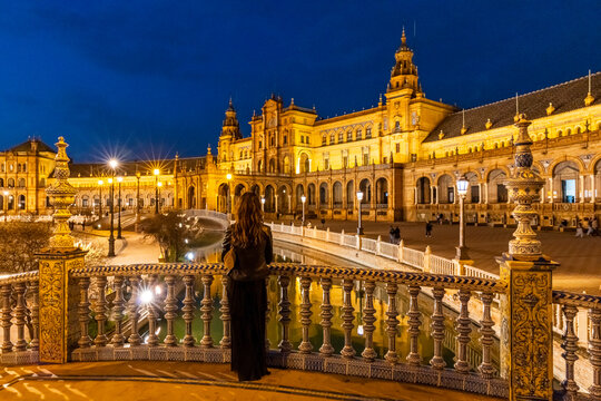 Travel, tourism: Woman looks at the illuminated Plaza de Espa&ntilde;a at night from a bridge, Seville, Spain.