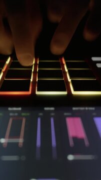 Close up of musician hands playing a rhythm on the illuminated pads of a midi controller. Concept of electronic music production, creative DJ workflow, and nightlife entertainment.