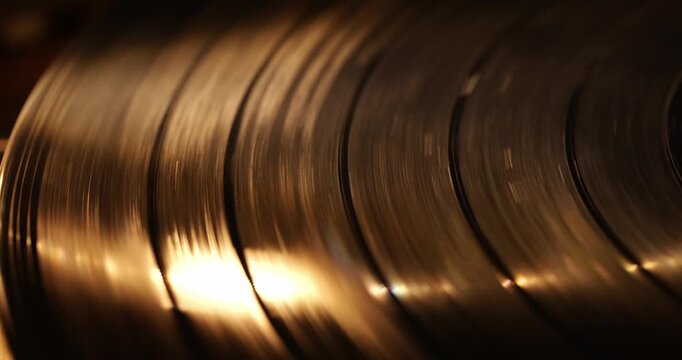 Close-up view of spinning vinyl records reflecting warm light, showcasing grooves and textures in a dimly lit environment, emphasizing the beauty of analog music