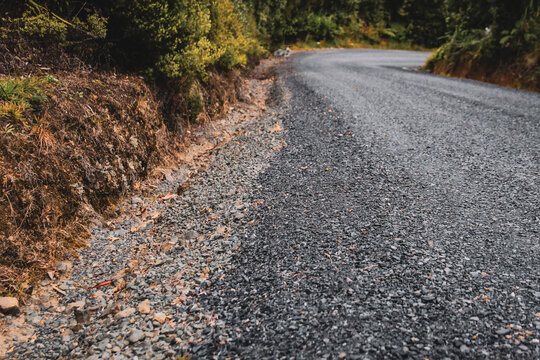 a road surfaced with gravel or crushed rock with a drainage swale or edge on the left. vegetation lines the edge. transportation background.