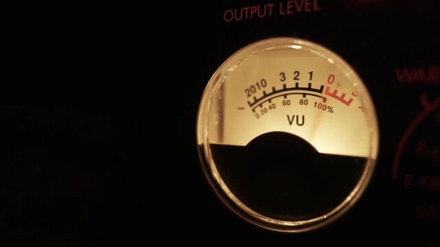 A close-up of a classic analog VU meter with its needle fluctuating to measure audio signal levels. Concept of music production, sound engineering, audio mixing, and vintage technology.