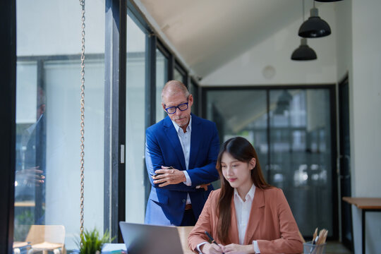 Business mentor watching young Asian woman working at laptop