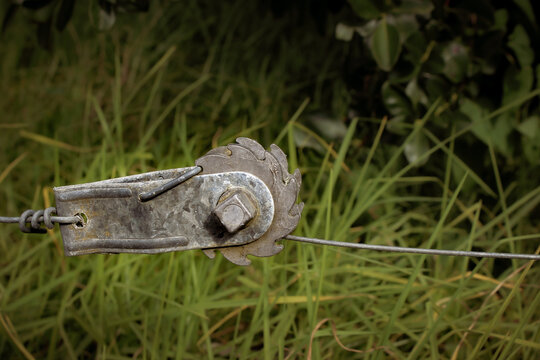 Macro closeup of a galvanized steel fence in-line wire tensioner, also known as a ratchet strainer, commonly used in agriculture and gardening