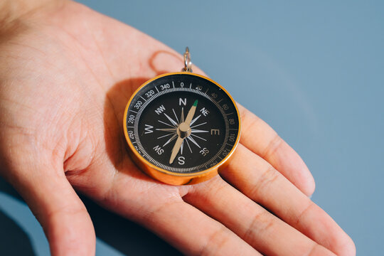 Compass rests on open palm, showcasing its detailed markings and needle pointing north. This symbolizes navigation, exploration, and guidance, evoking sense of adventure and direction