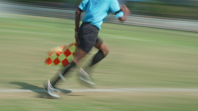Assistant referee captured mid stride running swiftly along sidelines with fluorescent shirt waving flag signaling call for players during match