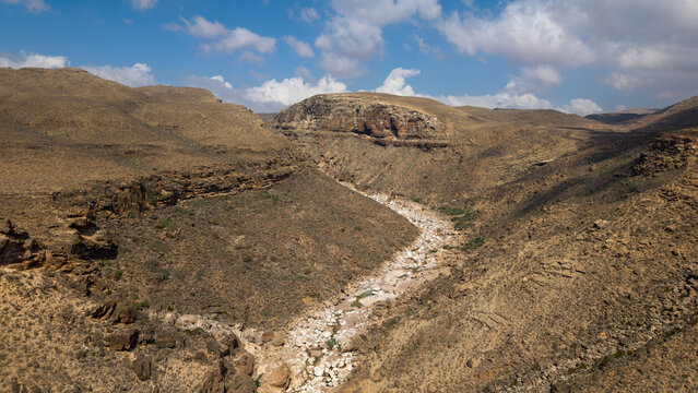 Desert canyon valley with dry riverbed under cloudy sky