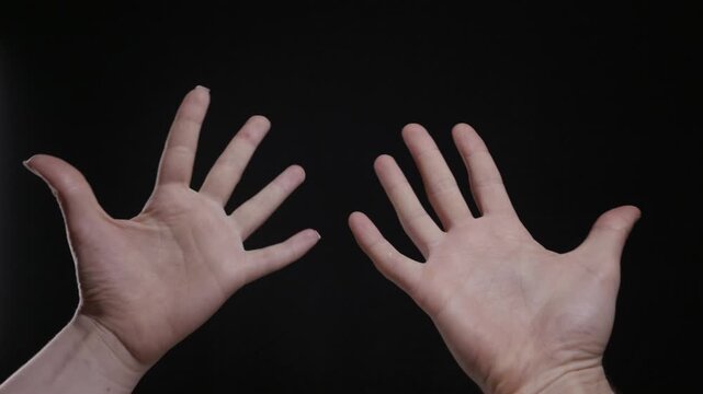 A close up of two hands with open palms rising into frame against a solid black background. Concept of surrender, openness, showing, or a simple human gesture and communication.