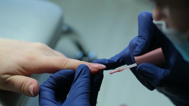 Applying Nail polish, pink shellac UV gel, varnish, manicure process concept in beauty salon. Transparent top coat drop on brush. Over pink background. Application of nail polish. High quality 4k