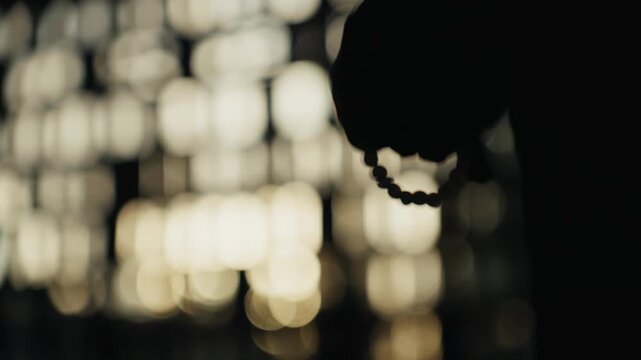 Silhouette of a person praying with rosary beads