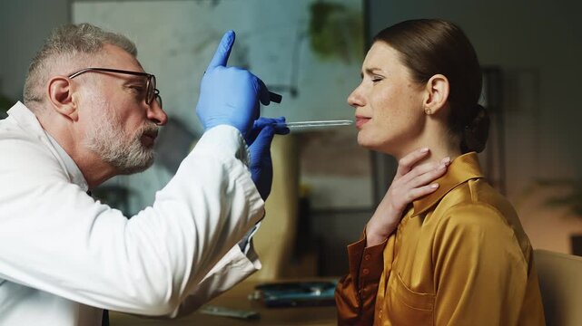 Man ENT doctor examining female patient's throat during medical checkup, virus