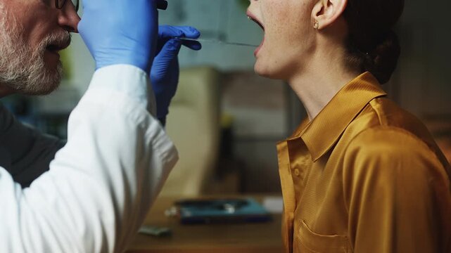 Male otolaryngologist examining young woman's throat in clinic, health check-up