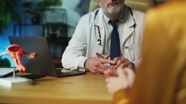 Middle-aged male obstetrician consulting female in clinic, regular check-up