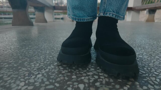 Person walking forward on patterned pavement wearing light blue jeans and black platform boots, creating a sense of movement, fashion, and urban exploration