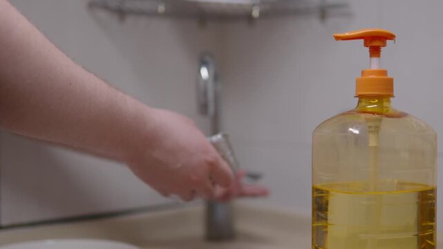Hands cleaning plates with a sponge and liquid soap from a dispenser bottle, illustrating the domestic chore of washing kitchenware and maintaining household hygiene
