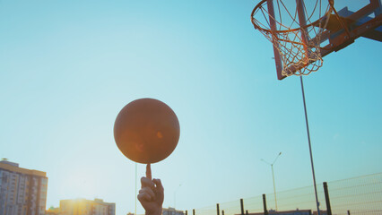 Man spinning basketball on finger against hoop and blue sky, have fun and enjoy © vla