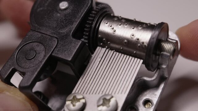 A pinned metal cylinder rotates against a steel comb inside a mechanical music box to produce melody. The movement illustrates precision engineering and vintage analog entertainment.