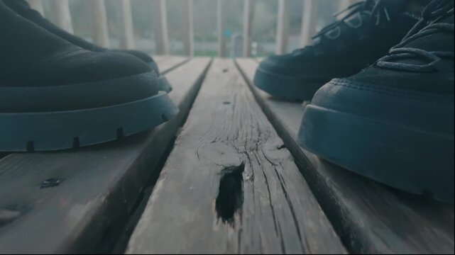 People standing on weathered wooden deck with sturdy boots and shoes, creating a low angle perspective showing the footwear and textured planks against an outdoor background