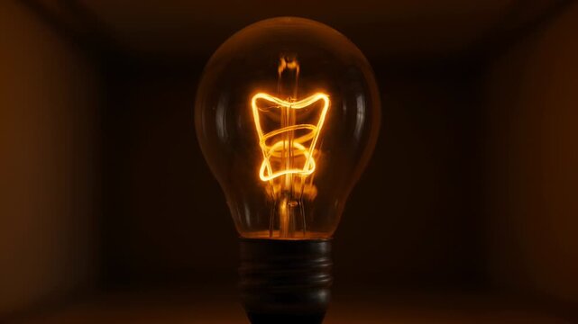 Light bulb filament glowing brightly in warm tones, transitioning from illuminated to dim, showcasing the gradual change in brightness and visual intensity within a dark setting
