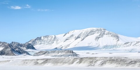 Naklejka premium Snowy mountains dominate landscape. White peaks contrast with blue sky. Frozen terrain extends toward horizon. Quiet, remote beauty.