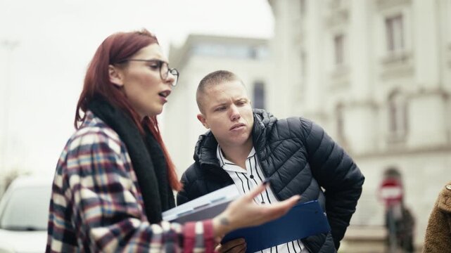 Young professionals engage in a focused business discussion outdoors, reviewing documents and strategizing. Two colleagues communicate and collaborate on a project in an urban environment.