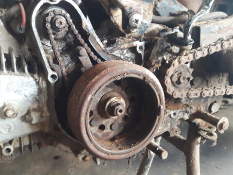 Detailed view of a disassembled vintage motorcycle engine with rusty magnetic rotor and timing chain in a garage.
