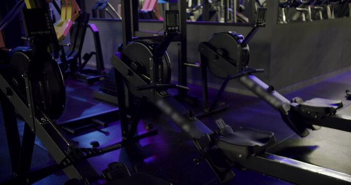 Empty fitness center with modern rowing machine simulators for intense cardio workout and strength training, illuminated by dramatic blue and purple neon lights for a motivating atmosphere