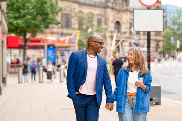 Couple walks hand in hand on a busy city street during the day in Manchester