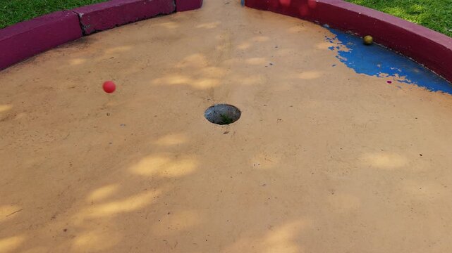 Woman aiming mini golf shot on outdoor tropical course with red ball resting on narrow pathway