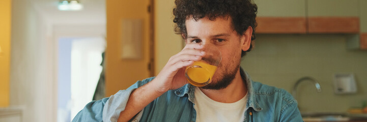 Fototapeta premium Guy dressed in denim shirt works on laptop while having lunch in cozy kitchen. Panoramic