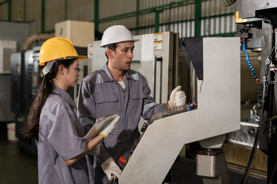 Asian woman technician studies tablet beside adult male operator at CNC station, reviewing machine condition, control status, and production workflow for safe manufacturing operations each day