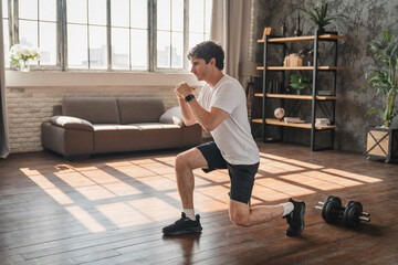 Active Caucasian man doing forward lunges during fitness workout at home. Young athletic sportsman...