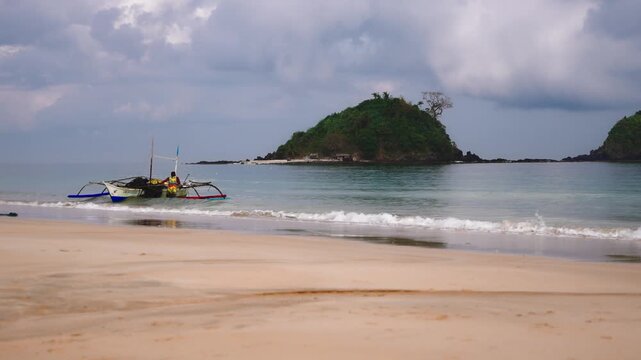 Traditional Filipino bangka boat floating in shallow turquoise water near a small tropical island off Nacpan Beach in El Nido Palawan Philippines.