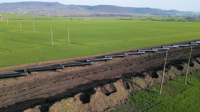 Aerial panoramic view of Balkan Stream gas pipeline project in Bulgaria. Long row of steel pipes laid out for installation across green agricultural fields and rural landscape