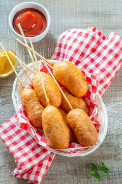 Eating corn dogs at a summer fair with friends while enjoying dipping sauces in the afternoon sun
