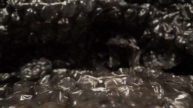 Close up dolly slider shot moving across black bubble wrap packaging material with reflective plastic texture and shallow depth of field. Abstract macro view of protective packing film surface with gl
