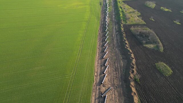 Top-down aerial view of the Balkan Stream gas pipeline construction in Bulgaria. Steel pipes laid in a row between green agricultural fields and plowed soil