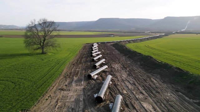 Aerial panoramic view of Balkan Stream gas pipeline project in Bulgaria. Long row of steel pipes laid out for installation across green agricultural fields and rural landscape