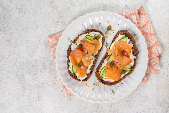 Sliced bread topped with smoked salmon, cream cheese, and cucumber on a white plate at a kitchen table