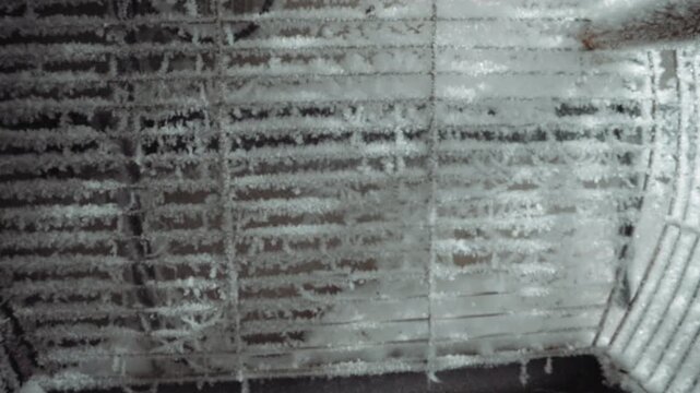 Frostcovered reactor grate interior, icy metal ribs and sootstained slats show nuclear winter aftermath, drone inspection perspective reveals layered frost, rust, and sediment on industrial vent,