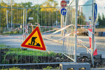 Road construction warning sign, metal fence blocking street, barrier tape, temporary fencing around...