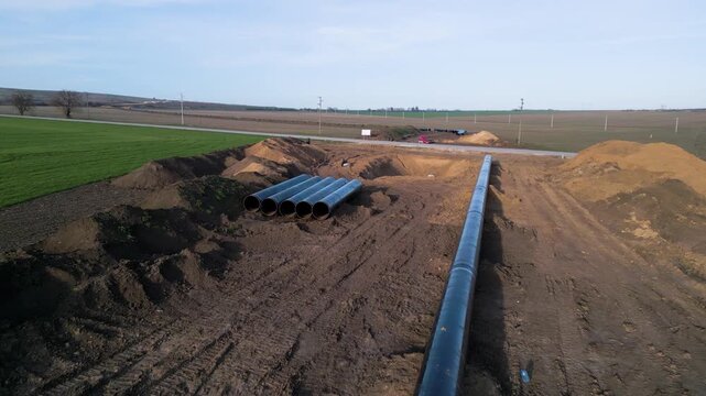 Ground-level perspective of steel pipes for the Balkan Stream gas pipeline in Bulgaria. Row of large diameter tubes on a construction site across green fields under a clear sky