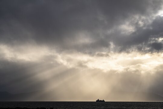 Silhouette of a ship, sun rays breaking through the cloud cover, Ullsfjord, Lyngen, Troms og Finnmark, Norway