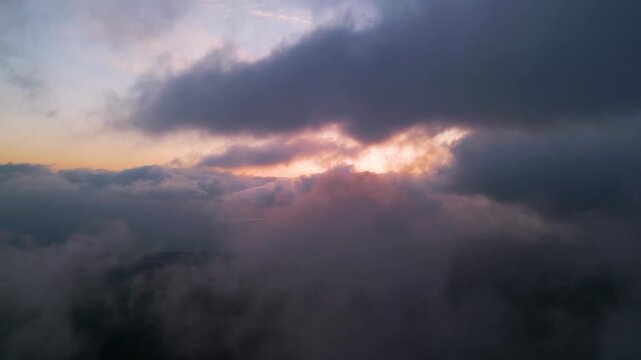 Dramatic aerial sunset view through heavy clouds. Golden light breaking through dark storm clouds, creating a moody and atmospheric nature background