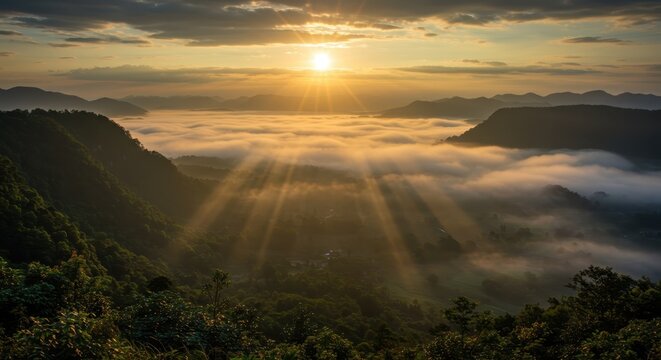Brilliant sunbeams pierce through morning mist settled over forested mountain valleys.