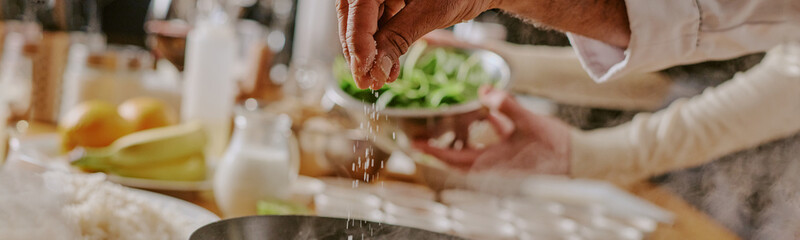 Website banner of unrecognizable man sprinkling salt into pan during cooking class while woman...