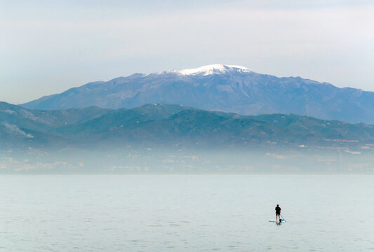 Cold weather at the Costa del Sol in winter; man on sup board with snowcapped Maroma mountain in background