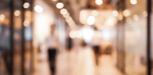 A blurred view of a modern shopping mall with warm lighting, featuring people walking and a vibrant atmosphere, capturing the essence of urban retail spaces.