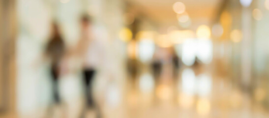 A blurred image of people walking in a modern indoor space, likely a shopping mall or office corridor, with warm lighting creating a soft atmosphere.