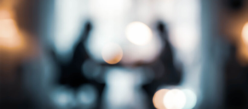 An abstract image featuring silhouettes of two people engaged in conversation or discussion in a softly blurred setting with warm light bokeh.