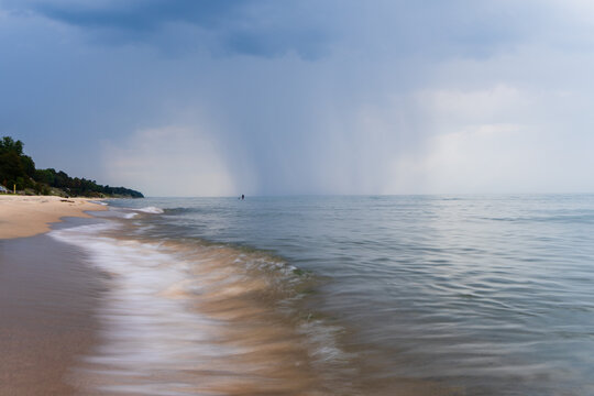 Rain shafts over Lake Michigan with waves along sandy shoreline